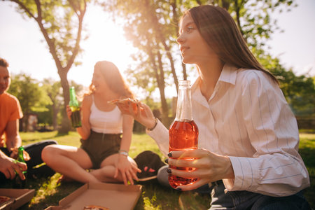 Young girl drinking alcohol and eating pizza with her friends outdoors, background image, focus on foregroundの写真素材