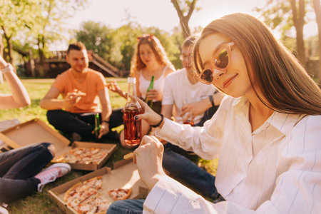 Young girl drinking alcohol and eating pizza with her friends outdoorsの写真素材