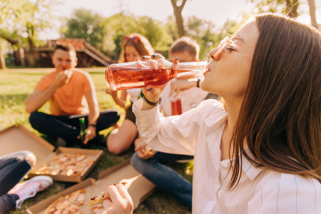 Young girl drinking alcohol and eating pizza with her friends outdoorsの写真素材