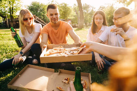 Five young cheerful people eating pizza and drinking beer outdoorsの写真素材