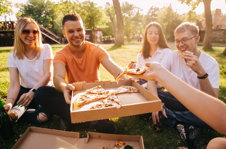 Four young cheerful friends eating pizza outdoorsの写真素材