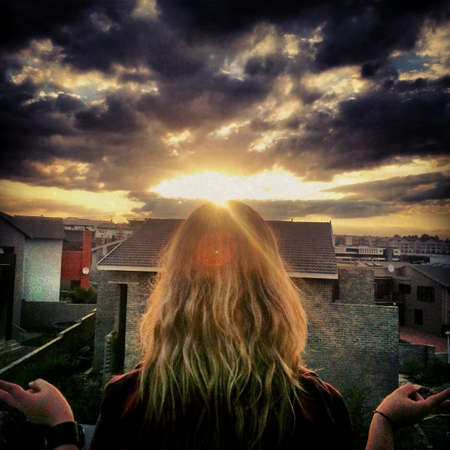 Girl sitting on the top of the roof looking at the sunset の素材