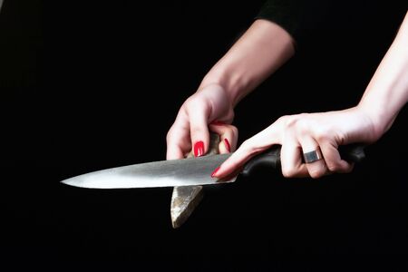 female hands are sharpening knife on the blackの写真素材