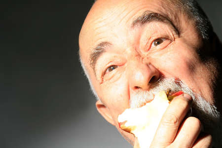face shot og a senior gentleman with apple in mouthの写真素材