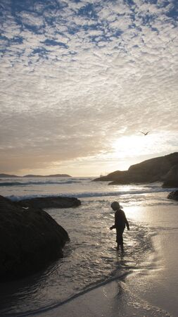 A boy near the water at low tide at sunset.の写真素材