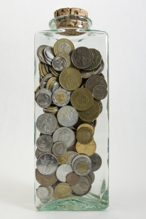 A glass jar filled with coins from a variety of countries isolated on a white background   の写真素材