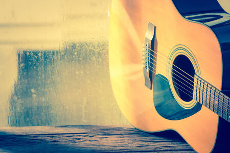 Acoustic guitar next the window with drop waterの写真素材