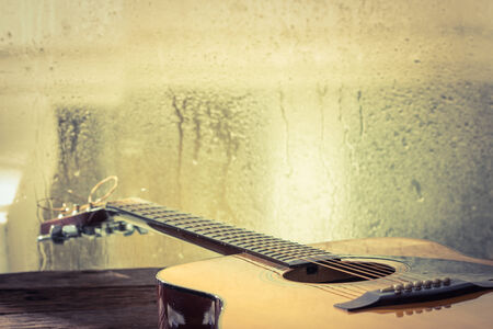 Acoustic guitar next the window with drop waterの写真素材