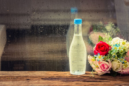 Cold water in bottle with flowers on wood table.beside glass window