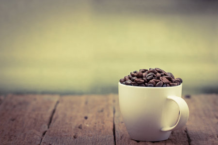 Cup full of coffee beans on wood tableの写真素材