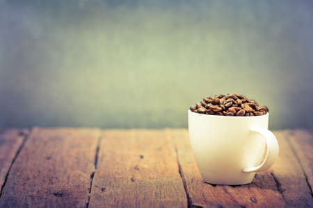 Cup full of coffee beans on wood tableの写真素材