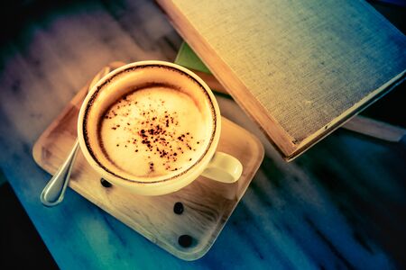 Cup of cappuccino coffee and books on wooden tableの写真素材