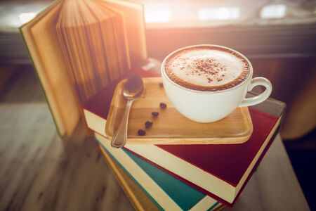 Cup of cappuccino coffee and books on wooden tableの写真素材