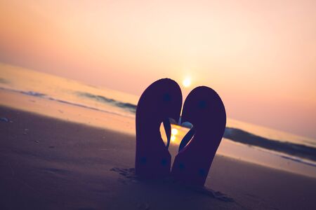 Silhouette slippers is tilted of love on  sandy ocean and sunset  or sunrise beachの写真素材