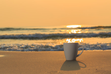 Close up white coffee cup on sand beach and view of sunset or sunrise background,peacefulの写真素材