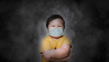 Little boy in a disposable mask with dust and smoke background. Asian kid is wearing the mask for protect them self from virus and air pollution.の写真素材