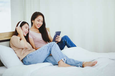 Couple women relaxing on bed using digital tablet for video callの写真素材