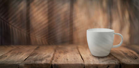 Cup of coffee with shadow tropical leaves on wood backgroundの写真素材
