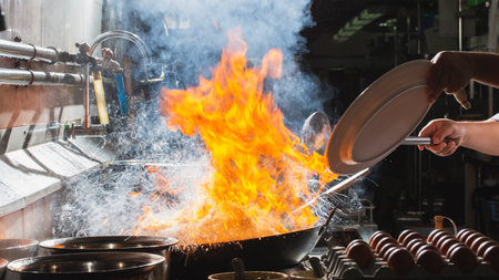 Chef stir fry busy cooking in kitchen. Chef stir fry the food in a frying pan, smoke and splatter the sauce in the kitchen.の写真素材