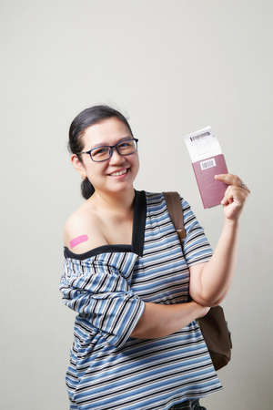 Asian woman ready for safe travel journey. Portrait of happy holding passport, smiling and showing arms after receiving vaccine.の写真素材
