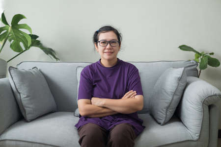Asian woman middle-aged smiling portrait sitting on the sofa in houseの写真素材