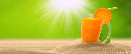 Orange juice on sand with greenery background, copy spaceの写真素材
