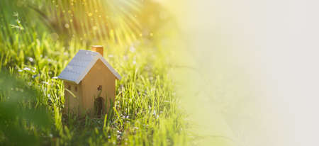 House wood model with copy space of home and life concept. Model home on green grass with sunlight abstract background. Banner size Photoの写真素材