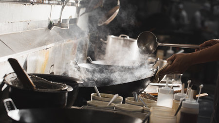 Chef stir fry busy cooking in kitchen. Chef stir fry the food in a frying pan, smoke and splatter the sauce in the kitchen.の写真素材