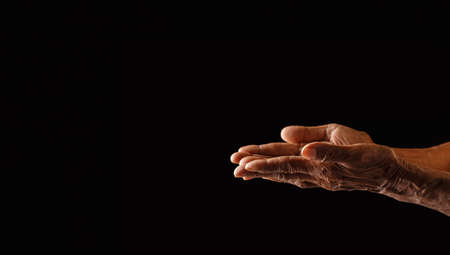 Wrinkled old man's hand with empty hand on dark background