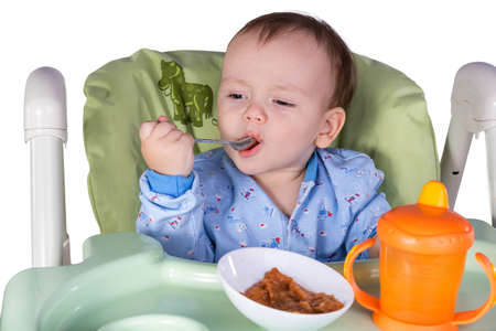 child is eating sitting at table, isolated over whiteの写真素材