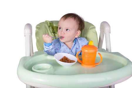 child is eating sitting at table, isolated over whiteの写真素材