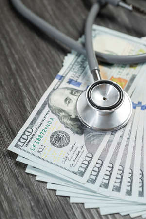 Stethoscope on top of hundreds banknote on black wooden table, focusing on Franklin's eyeの写真素材
