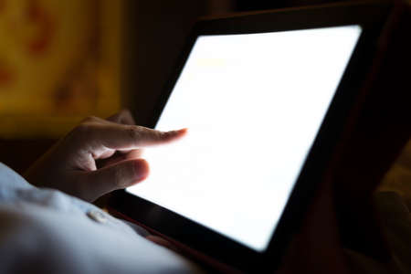 Closeup of female hand using tablet at night on bed