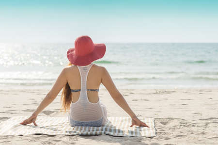 Unrecognizable Asian woman sitting on the beach with red hatの写真素材
