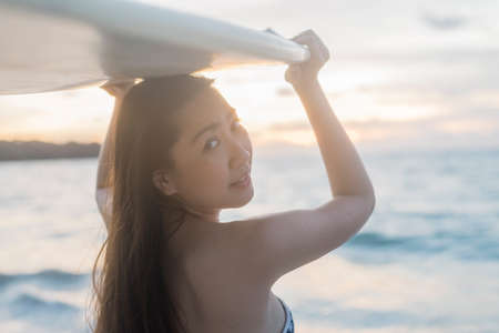 Thai woman holding surfboard on the evening beach