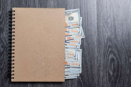 Money series : Hundred dollar banknotes in brown cover book on black wooden tableの写真素材