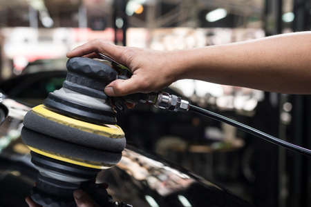 Car polishing series: Closeup of worker's hand using tool waxing black car hood in garageの写真素材
