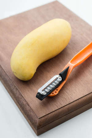 Fruits series : Yellow mango and peeler on wooden board