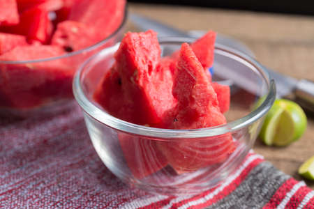 Fruits series : Sliced of watermelon in glass bowl on wooden plank table with knifeの写真素材
