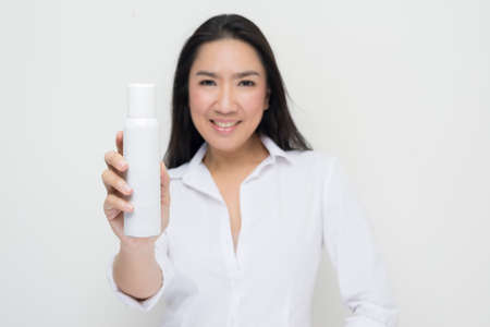 Beauty series: Asian woman holding white spray bottle against white backgroundの写真素材