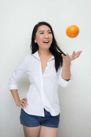 Fruits series: Asian woman throwing orange against white backgroundの写真素材