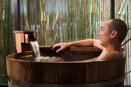 Onsen series: Asian man taking a bath in wooden bathtubの写真素材