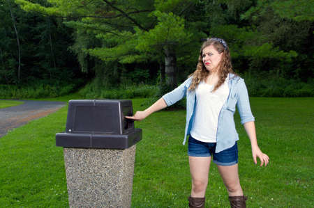 Teen Girl  in a park looking in a trash can with a disgusting look on her faceの写真素材