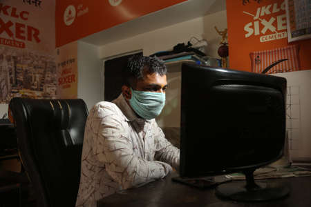 jodhpur, rajasthan, india, 20th September 2020: Focused Indian young male working on his computer wearing face mask, back to work,new normal. covid-19 pandemic.のeditorial素材