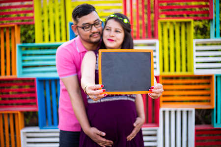 Young pregnant asian indian couple holding writing slate together, pregnancy concept. selective focus on slate.の写真素材