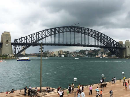 Sydney, Australia - Jan 6, 2018: Sydney Harbour bridge with Australian and Aboriginal flags and group of tourists on the bank.のeditorial素材
