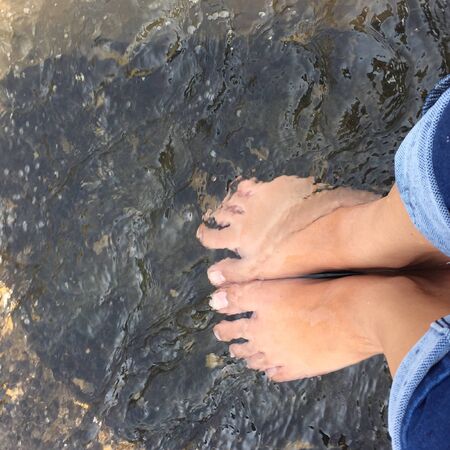 Top view of man's feet on the sand at the surf waves over them. Point of view on legs in sand with sea foam ocean summer background - Image,Vacation on ocean beach, feet on sea sand.の写真素材