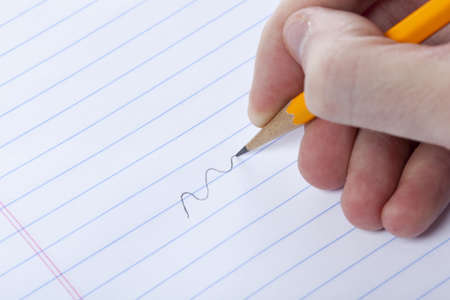 A person writing with a yellow pencil on notebook paperの写真素材