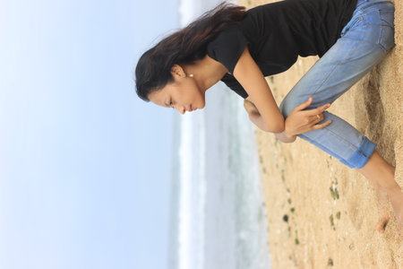 Young woman relaxing at the beach, she is leaning on a wall.