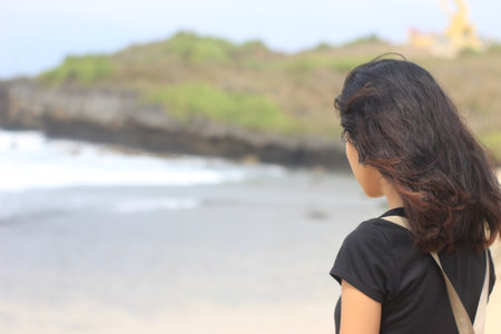 Young woman looking at the sea, view from the back, blurred backgroundの写真素材